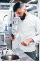 Chef in white uniform standing at kitchen. Holding knives in hands photo