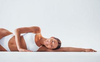 Lying down on the floor. Beautiful woman with slim body in underwear is in the studio photo