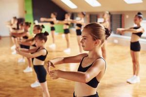 Standing in the row. Group of female kids practicing athletic exercises together indoors photo