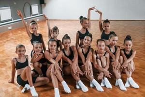 Posing for a camera. Group of female kids practicing athletic exercises together indoors photo