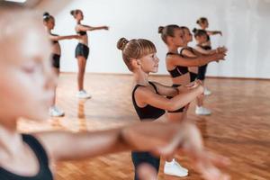 Standing in the row. Group of female kids practicing athletic exercises together indoors photo