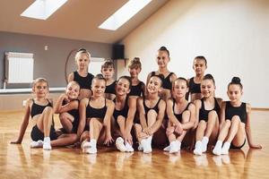 Posing for a camera. Group of female kids practicing athletic exercises together indoors photo