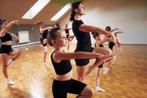 Learning from coach. Group of female kids practicing athletic exercises together indoors photo