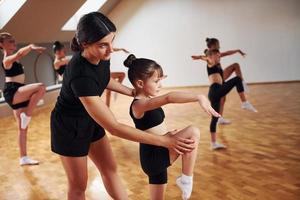 Learning from coach. Group of female kids practicing athletic exercises together indoors photo