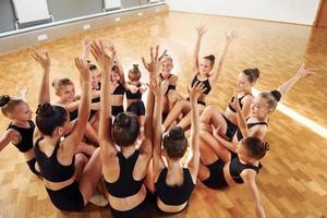 Many of people. Group of female kids practicing athletic exercises together indoors photo