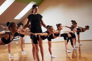 Coach is helping. Group of female kids practicing athletic exercises together indoors photo