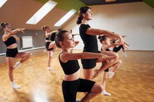 Learning from coach. Group of female kids practicing athletic exercises together indoors photo