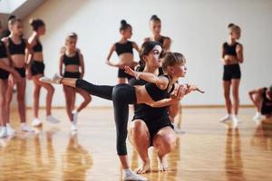 Woman teaching and helping. Group of female kids practicing athletic exercises together indoors photo