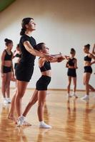 Woman teaching and helping. Group of female kids practicing athletic exercises together indoors photo