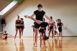 mujer enseñando y ayudando. grupo de niñas practicando ejercicios atléticos juntas en el interior foto