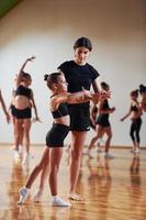 Woman teaching and helping. Group of female kids practicing athletic exercises together indoors photo