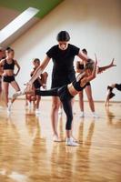 With help from coach. Group of female kids practicing athletic exercises together indoors photo