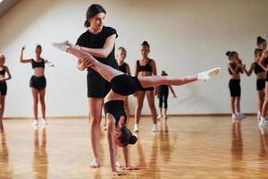 Woman teaching and helping. Group of female kids practicing athletic exercises together indoors photo