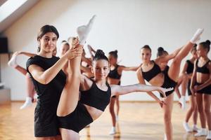 con la ayuda del entrenador. grupo de niñas practicando ejercicios atléticos juntas en el interior foto