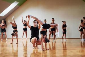 Adult coach is helping. Group of female kids practicing athletic exercises together indoors photo