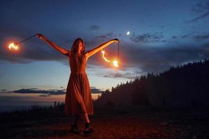 Fire show by woman in dress in night Carphatian mountains. Beautiful landscape photo