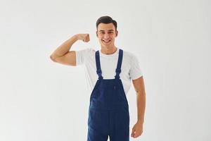 Shows biceps. Ready to work. Male worker in blue uniform standing inside of studio against white background photo