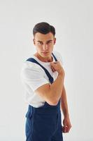 Shows biceps. Ready to work. Male worker in blue uniform standing inside of studio against white background photo