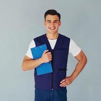 Holds notepad. Male worker in blue uniform standing inside of studio against white background photo