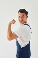 Shows biceps. Ready to work. Male worker in blue uniform standing inside of studio against white background photo