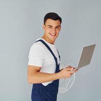Uses laptop. Male worker in blue uniform standing inside of studio against white background photo