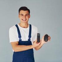 TV remote controller and computer mouse. Male worker in blue uniform standing inside of studio against white background photo