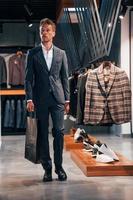 camina con la bolsa en la mano. chico joven en una tienda moderna con ropa nueva. ropa elegante y cara para hombres foto