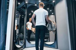 Guy in white shirt tries on new clothes and looks in the mirror photo