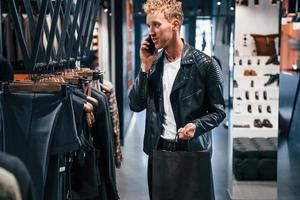 Talks by the phone. Young guy in modern store with new clothes. Elegant expensive wear for men photo