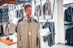 gran elección chico joven en una tienda moderna con ropa nueva. ropa elegante y cara para hombres foto