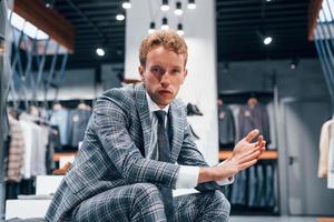 chico joven en una tienda moderna con ropa nueva. ropa elegante y cara para hombres foto