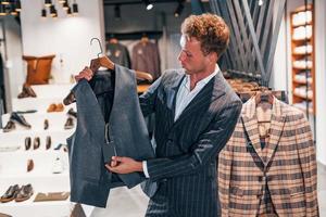 Shopping day. Young guy in modern store with new clothes. Elegant expensive wear for men photo