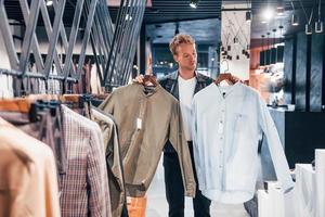 gran elección chico joven en una tienda moderna con ropa nueva. ropa elegante y cara para hombres foto