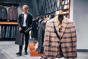 en hermosa chaqueta negra. chico joven en una tienda moderna con ropa nueva. ropa elegante y cara para hombres foto