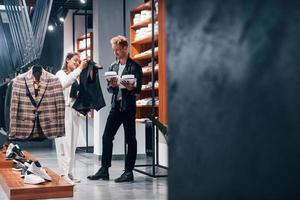 joven trabajadora ayudando a un chico a elegir ropa en una tienda moderna con ropa cara para hombres foto