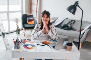 With laptop on the table. Young female freelance worker is indoors in home at daytime photo