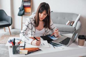 Sits by table. Young female freelance worker is indoors in home at daytime photo