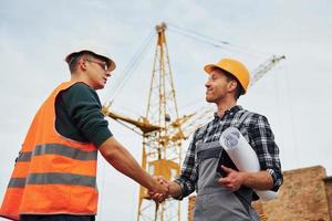 Making handshake. Two construction workers in uniform and safety equipment have job on building together photo