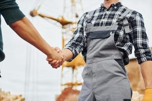 Making handshake. Two construction workers in uniform and safety equipment have job on building together photo
