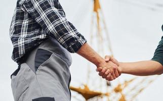 Making handshake. Two construction workers in uniform and safety equipment have job on building together photo