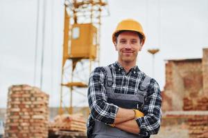 With arms crossed. Construction worker in uniform and safety equipment have job on building photo