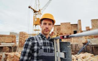 Ladder in hands. Construction worker in uniform and safety equipment have job on building photo