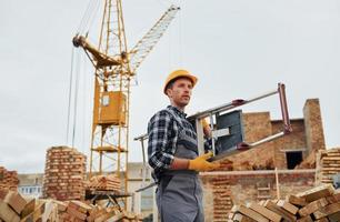 Ladder in hands. Construction worker in uniform and safety equipment have job on building photo