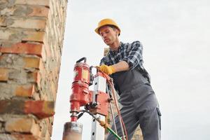 Uses blending drill. Construction worker in uniform and safety equipment have job on building photo