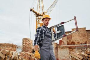 Ladder in hands. Construction worker in uniform and safety equipment have job on building photo