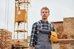 Hard hat and case in hands. Construction worker in uniform and safety equipment have job on building photo