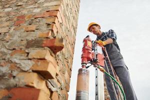 Uses blending drill. Construction worker in uniform and safety equipment have job on building photo