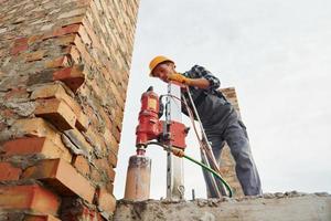 utiliza un taladro de mezcla. trabajador de la construcción en uniforme y equipo de seguridad tiene trabajo en la construcción foto