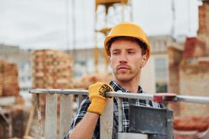 Ladder in hands. Construction worker in uniform and safety equipment have job on building photo