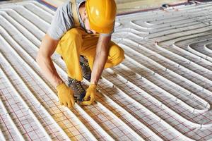 Worker in yellow colored uniform installing underfloor heating system photo